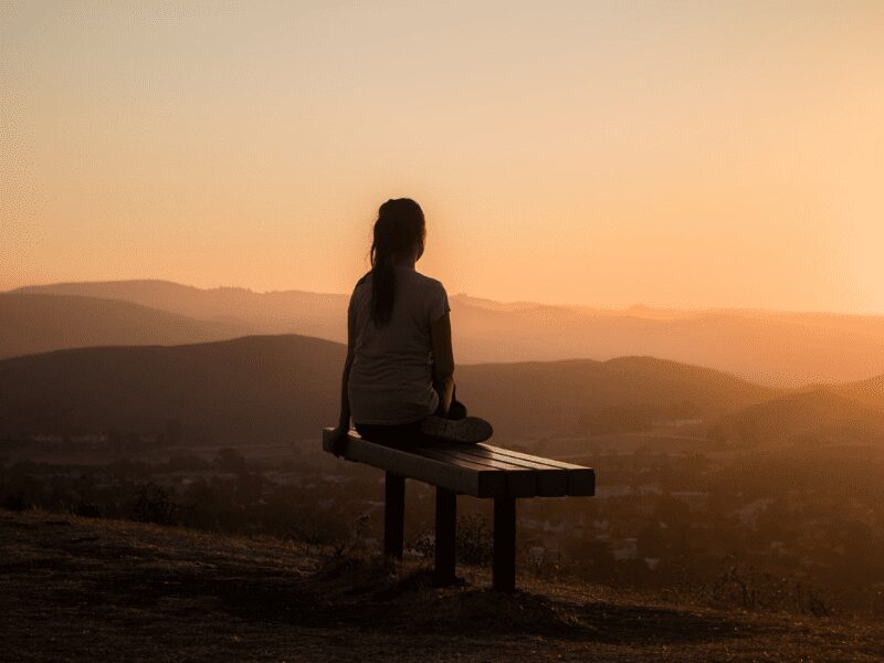 Grief And The Power Of Connection - Woman sitting lonely in a bench, watching the sunset