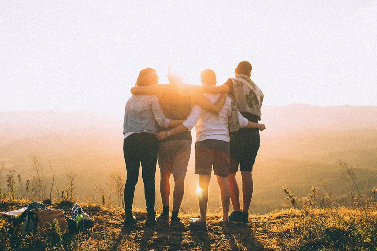 Four friends watching a sunrise together, holding each other. Find self-help and individual counseling through the guidely community app.