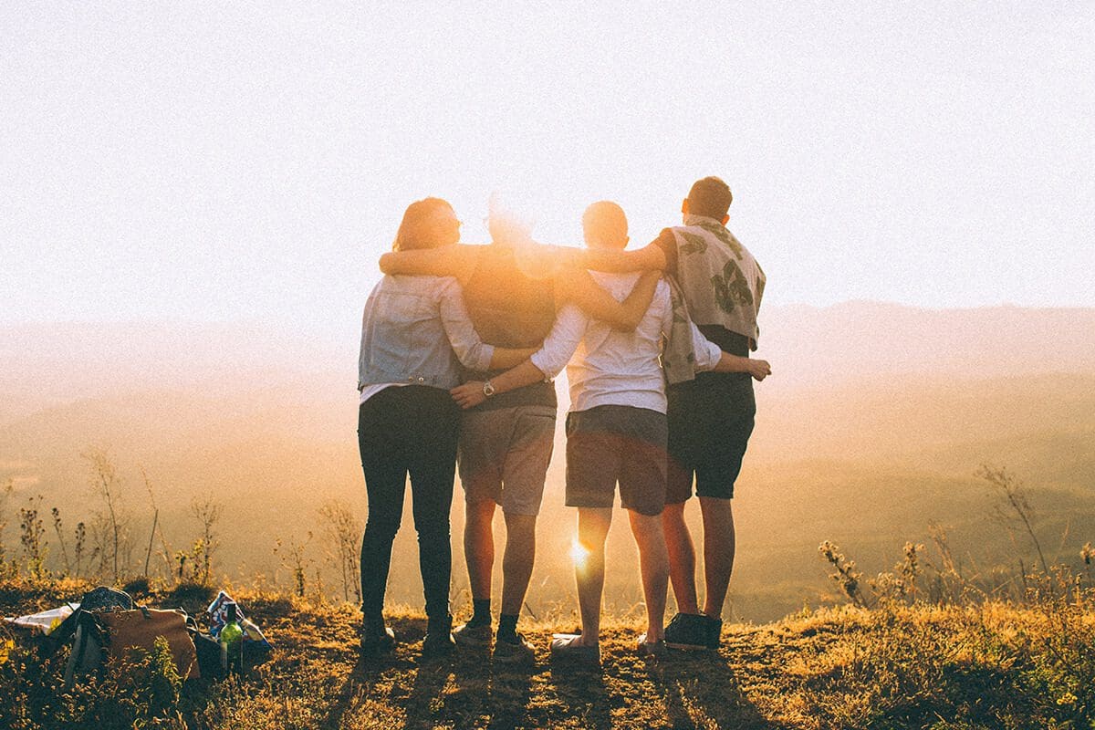 Four friends watching a sunrise together, holding each other. Find Self-Help and Individual Counseling through the Guidely Community app.