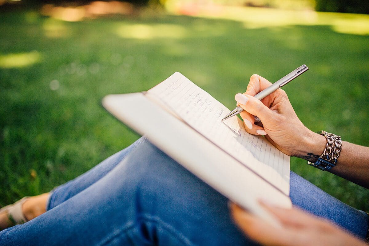 Person sitting outdoors, under the sun, journaling. 5 quick stress hacks for the month of may