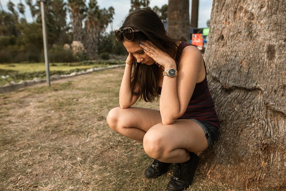 Woman sitting by a tree, feeling overwhelmed with stress.