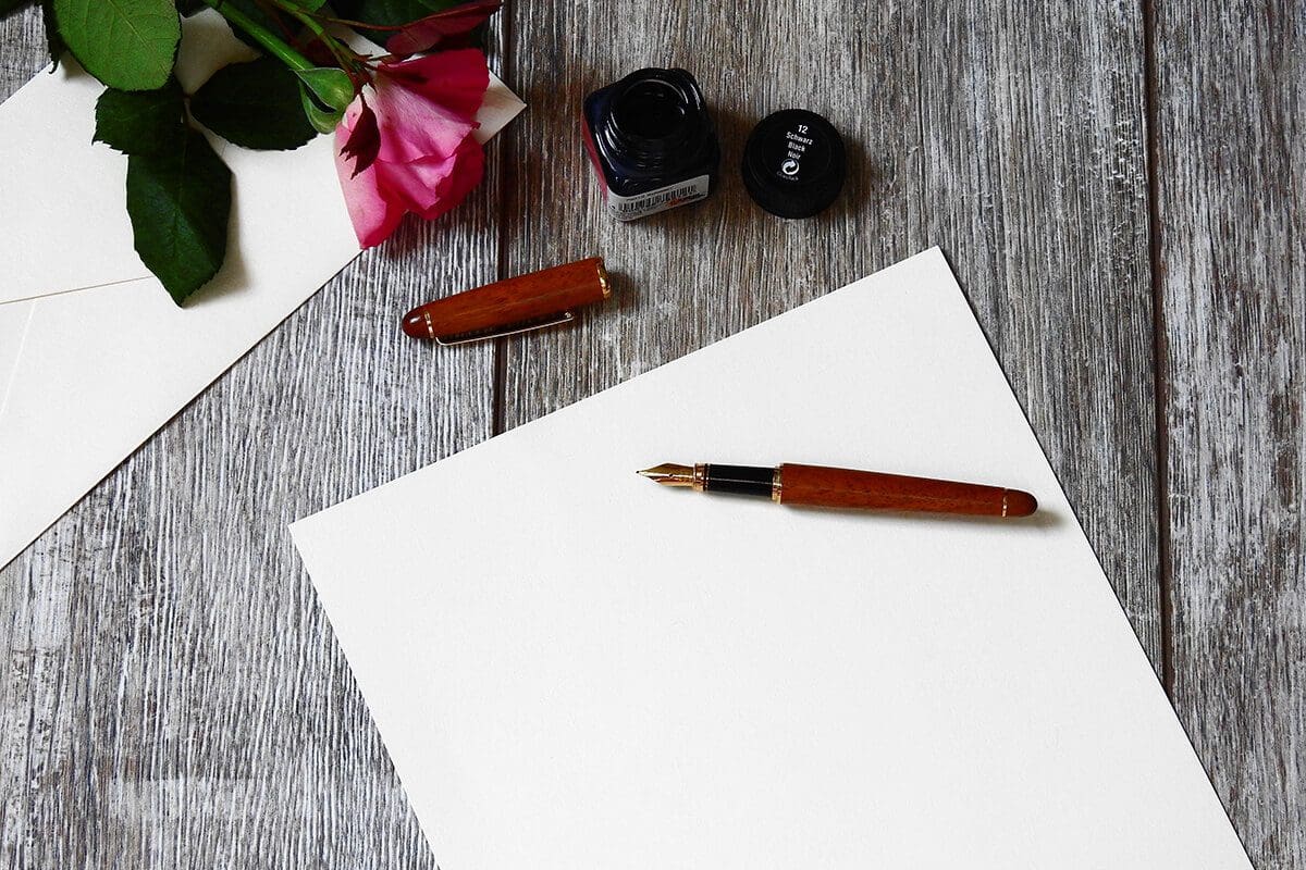 Write your next chapter with these 5 elements - image has a blank paper on a desk, with a pen on top ready to start writing.