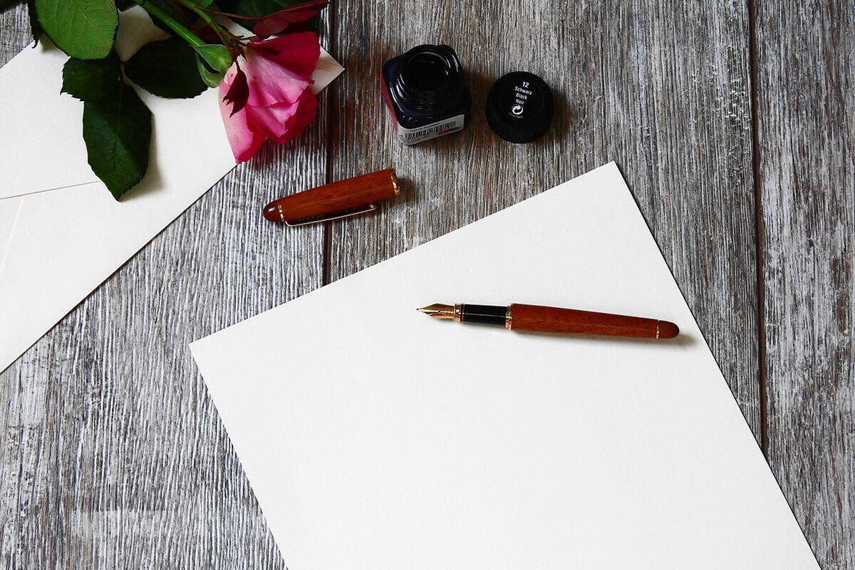 Write Your Next Chapter with these 5 Elements - Image has a blank paper on a desk, with a pen on top ready to start writing.