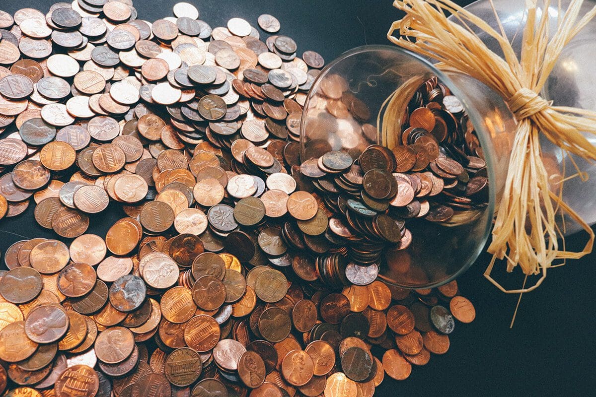 Riches and wealth: improving your money mindset - image in the background shows a jar with hundreds of pennies.
