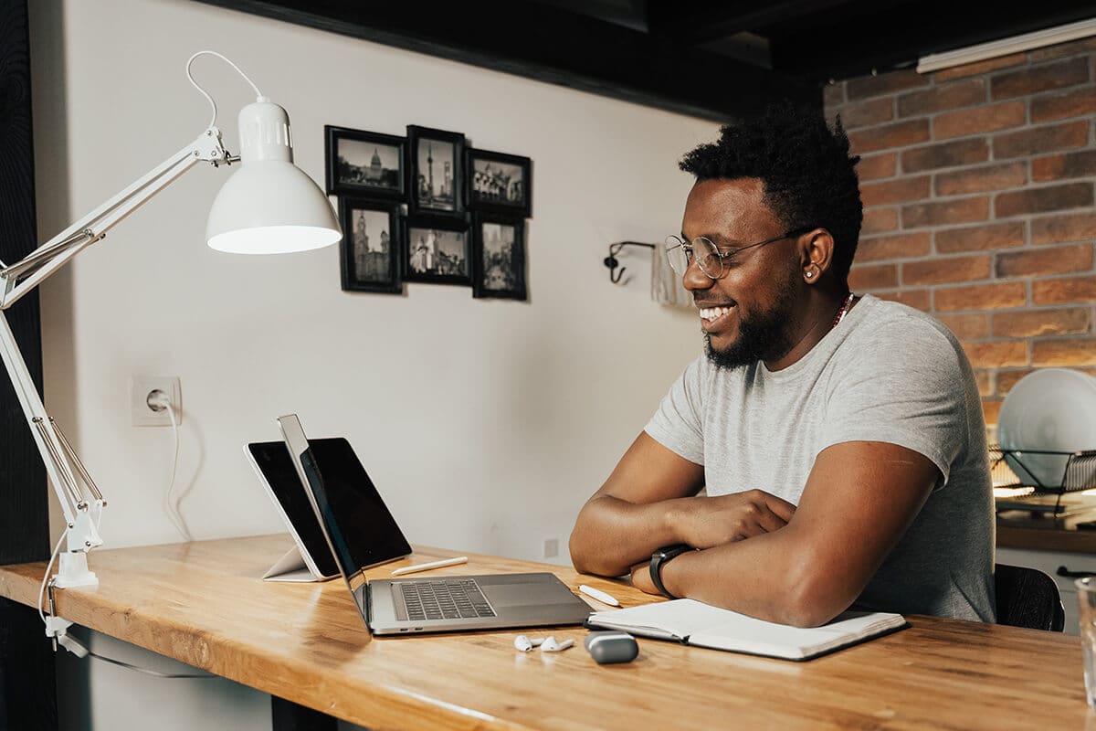 Ways to Start a Coaching Business: Man smiling at a computer screen while sitting on a desk.