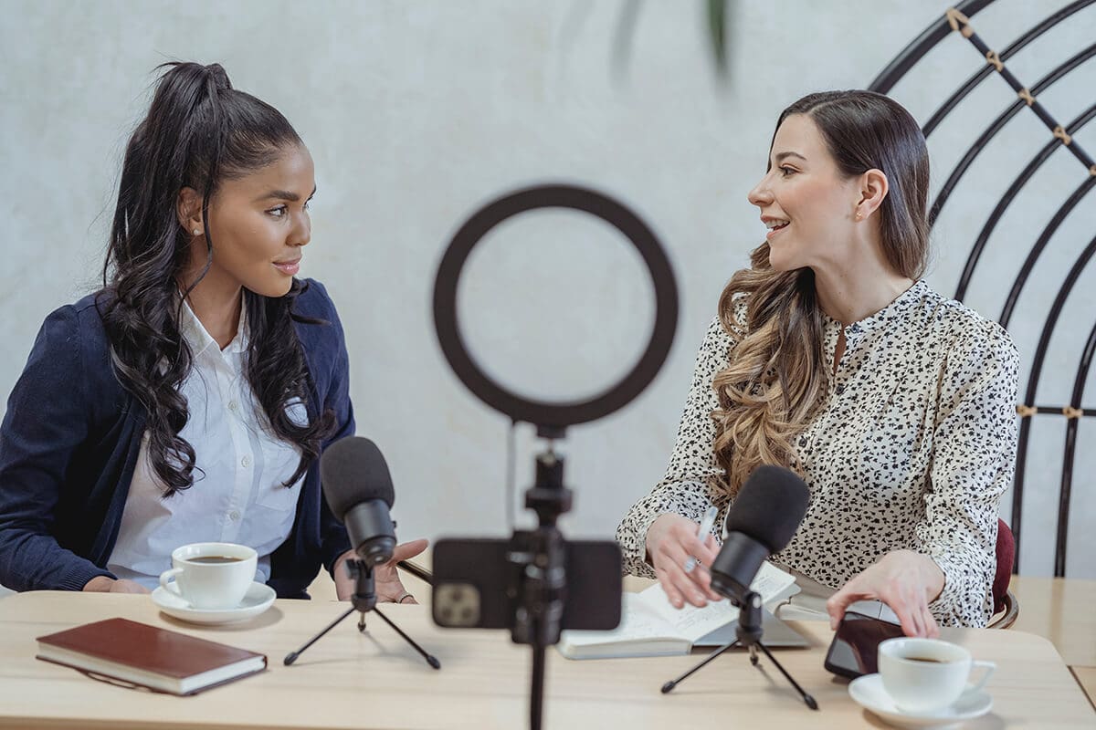 11 affordable marketing ideas for life coaches - two women speaking in front of a light and camera, recording a podcast.